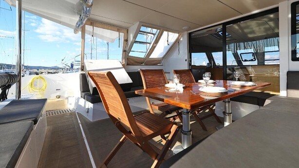 A dining area with a table set for four, surrounded by wooden chairs, on a boat deck with a view of the marina. - Sun-Kissed Sailing Adventure in Istria, Croatia (Pula)
