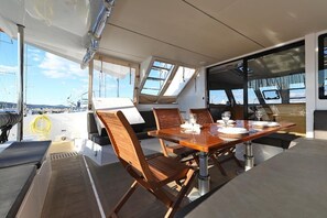 A dining area with a table set for four, surrounded by wooden chairs, on a boat deck with a view of the marina. - Sun-Kissed Sailing Adventure in Istria, Croatia (Pula)