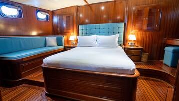 Una habitación con paneles de madera, una cama, un banco tapizado en azul y dos lámparas de noche.