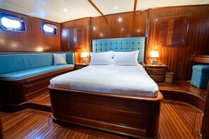 A wooden-paneled room with a bed, a blue upholstered bench, and two bedside lamps.