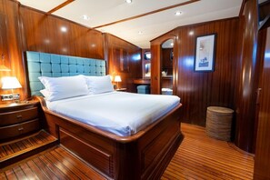 A wooden-paneled bedroom with a tufted headboard, a bed with white linens, a nightstand with a lamp, and a small waste bin.
