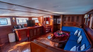 A boat interior with a wooden deck, a seating area with cushions, a coffee station, and a television. - Sun-Kissed Sailing Adventure in Islas Sarónicas (Alimos)