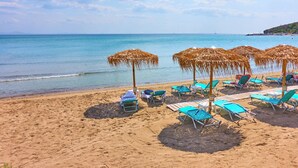 A beach with sun loungers and thatched umbrellas, a sandy shore, and calm sea.