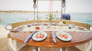A dining table on a boat with plates of food, glasses, and a vase with flowers.