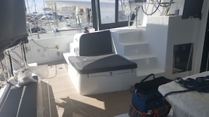 A boat's deck with a cushioned seating area, a small table, and a window.