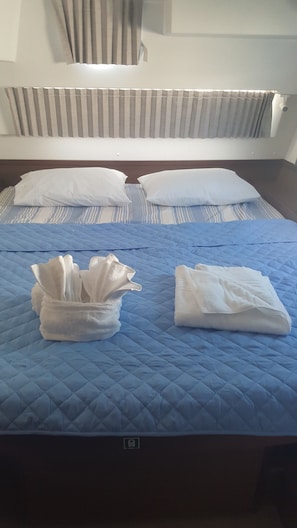 A bed with a blue quilt, two pillows, and two folded towels.