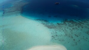 An aerial view of a beach with clear turquoise waters, a boat in the distance, and a sandy area. - Malé Marvel: Sun-Kissed Sailing Experience in the Maldivian Atoll (Hulhumalé)