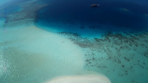 Eine Luftaufnahme eines Strandes mit klarem türkisblauem Wasser, einem Boot in der Ferne und einem Sandbereich.