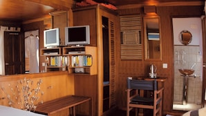 A wooden room with a bed, a small desk, a television, and a bathroom with a sink and mirror. - Malé Marvel: Sun-Kissed Sailing Experience in the Maldivian Atoll (Hulhumalé)