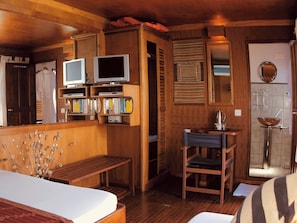 Ein Zimmer mit Holzboden, einem Bett, einem kleinen Schreibtisch, einem Fernseher und einem Badezimmer mit Waschbecken und Spiegel.