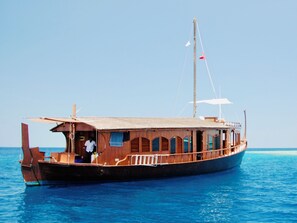A wooden boat with a cabin and a flag, floating on clear blue water.