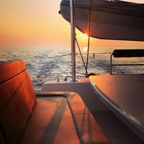 Ein Bootsdeck mit gepolsterten Sitzgelegenheiten, einer Reling und Blick auf den Ozean bei Sonnenuntergang.