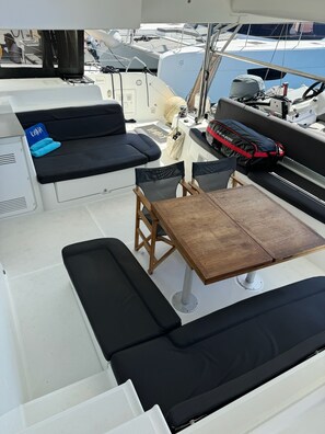 Cubierta de barco con zona de estar, una mesa y un timón.