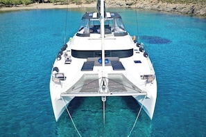 Eine weiße Yacht mit überdachtem Heck, klares blaues Wasser und eine felsige Küstenlinie im Hintergrund.