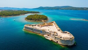 A coastal fortification with a circular structure, surrounded by clear blue waters and a small island with dense greenery. - Sibenik Sunshine Sailing: A Luxurious Croatian Beach Experience (Sibenik)