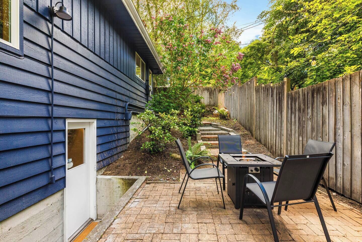 Een terras met vuurkorf, stoelen en een kleine tuin.