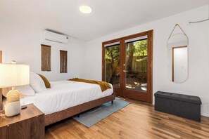 Een slaapkamer met een bed, nachtkastje, lamp, airconditioning en een spiegel, en een schuifpui.
