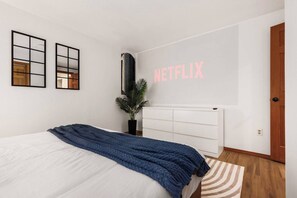 A bedroom with a bed, a potted plant, a radiator, and a wall with the word 'NETFLIX' in pink letters. - Lake City Downstairs 2BR • Movie Nights + Fireplace (Seattle)