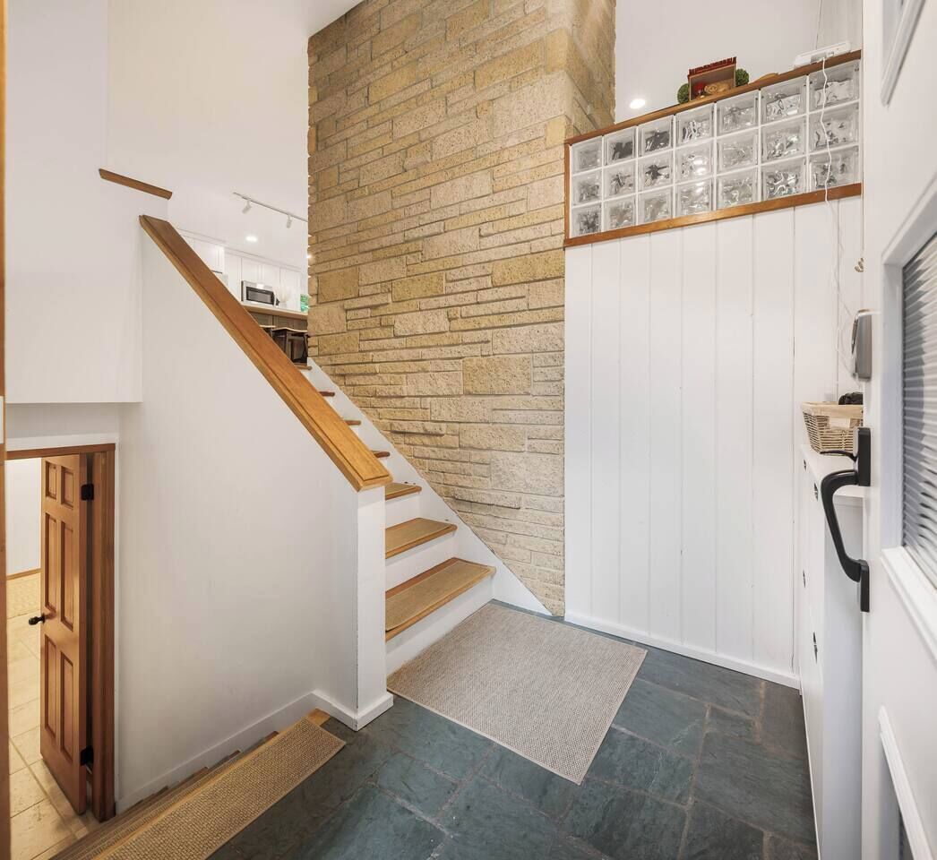 Una escalera de madera que conduce a una habitación con paredes blancas y piso de baldosas.