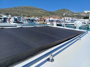 Ein Yachthafen mit vertäuten Booten, ein überdachter Bereich auf einem Boot und eine gebirgige Kulisse.