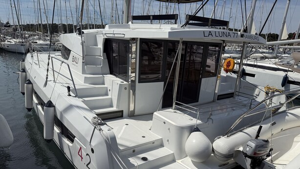 En hvid båd ved navn 'LA LUNA 77' ligger til kaj i en havn med flere andre både.