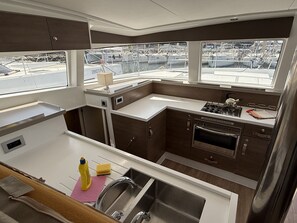 A compact galley kitchen with a stainless steel sink, a stove, and a view of the marina through the windows. - Sun-Kissed Sailing Adventure in Istria, Croatia (Pula)