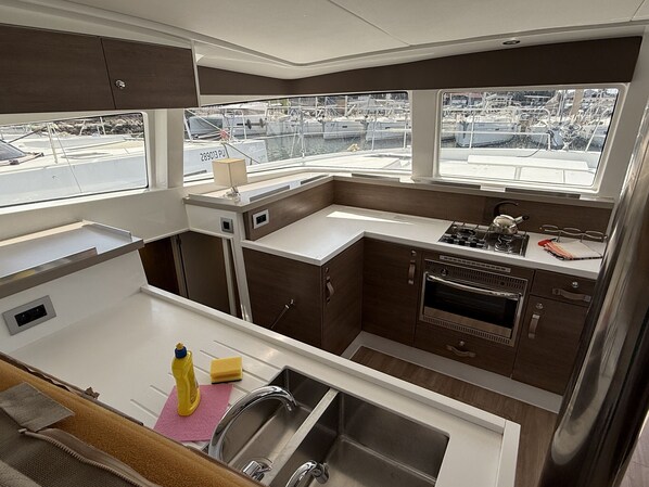A compact galley kitchen with a stainless steel sink, a stove, and a view of the marina through the windows.