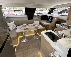A compact kitchen area with a dining table set for four, a small sink, and a stove. - Sun-Kissed Sailing Adventure in the Ionian Islands, Lefkada (Lefkada)