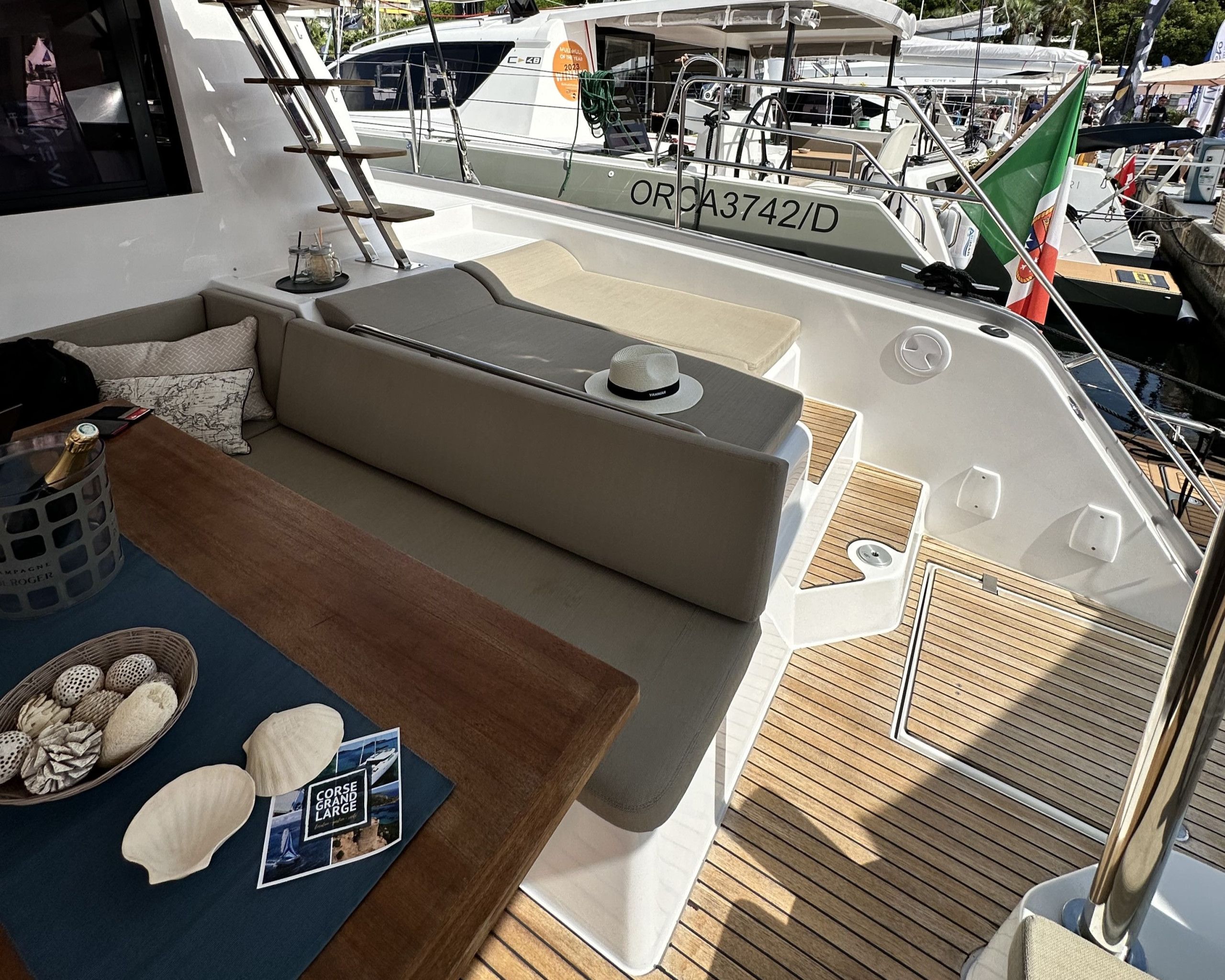 A yacht's deck with a seating area, a table with a bottle and glasses, and a brochure.