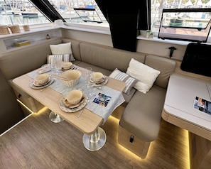 A yacht interior with a dining area, seating, and a view of the marina. - Sun-Kissed Sailing Adventure in the Ionian Islands, Lefkada (Lefkada)