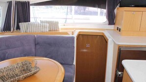 Interior compacto de una caravana con asientos acolchados, una mesita y una kitchenette.