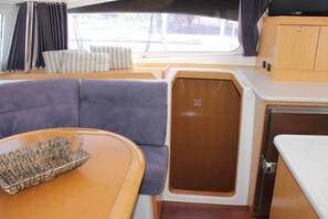 A compact RV interior with a cushioned seating area, a small table, and a kitchenette. - Sun-Kissed Sailing Adventure in Islas Sarónicas (Alimos)