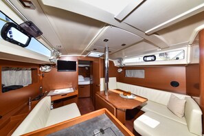 A compact interior with a bed, seating area, and a small table with a tray. - Sun-Kissed Sailing Adventure in Zadar, Croatia (Bibinje)