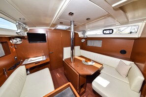 Un interior compacto con una mesa pequeña, asientos acolchados, un televisor y una ventana.