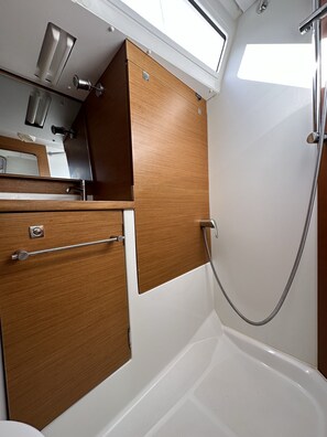 A bathroom with a shower, a mirror, and wooden cabinetry. - Sun-Kissed Sailing Adventure in Zadar, Croatia (Drage)