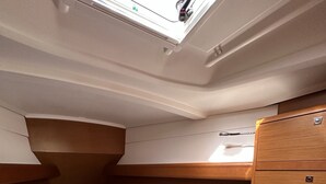 Cabine compacta e bem iluminada com beliche, um pequeno armário de madeira e um claraboia.
