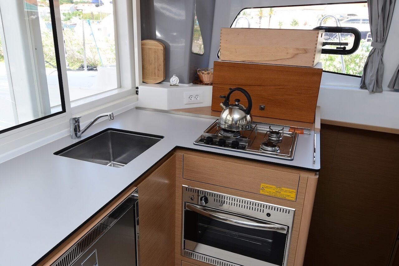 A compact kitchenette with a sink, stove, and oven, wooden cabinetry, and a window with a view of the outside.