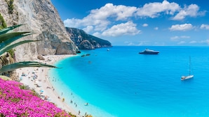 A coastal beach with clear turquoise waters, a rocky cliff, and a sailboat. - Sun-Kissed Sailing Adventure in the Ionian Islands, Lefkada (Lefkada)