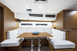 A compact interior with a central table, cushioned seating, and a window. - Sun-Kissed Sailing Adventure in Islas Sarónicas (Alimos)