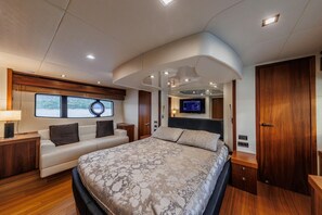 A modern bedroom with a bed, a sofa, a TV, and a window overlooking a body of water.