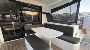 Un intérieur moderne et épuré, avec un espace salon comprenant une table blanche et des bancs noirs rembourrés, de grandes fenêtres offrant une vue sur le paysage urbain, et une porte coulissante donnant sur un espace extérieur.