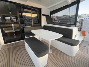 Um interior compacto e moderno com área de estar, incluindo uma mesa branca e bancos acolchoados pretos, grandes janelas com vista para a cidade, e uma porta deslizante que dá para um espaço ao ar livre.