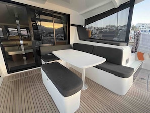 A compact, modern interior with a seating area featuring a white table and black cushioned benches, large windows offering a view of the cityscape, and a sliding door leading to an outdoor space.