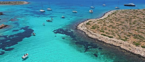 Eine Küstenlandschaft mit Booten, klarem türkisblauem Wasser, felsigem Gelände und einer kleinen Insel.