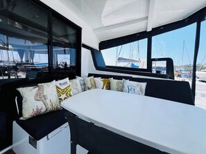 Ein Bootinnenraum mit Essbereich, gepolsterten Sitzgelegenheiten und Blick auf den Hafen.