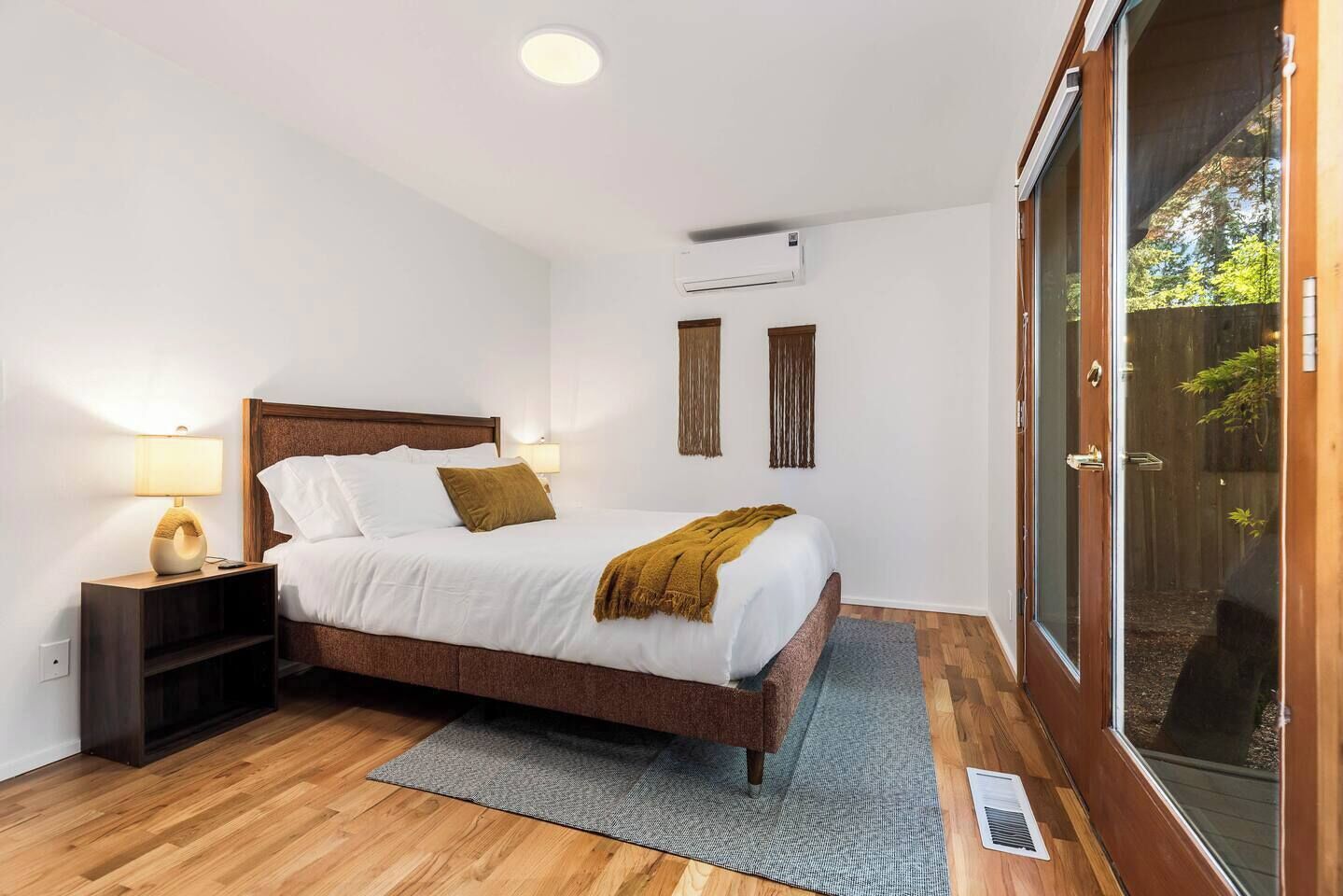 A bedroom with a bed, bedside lamps, a wooden headboard, a grey rug, and a wooden floor.