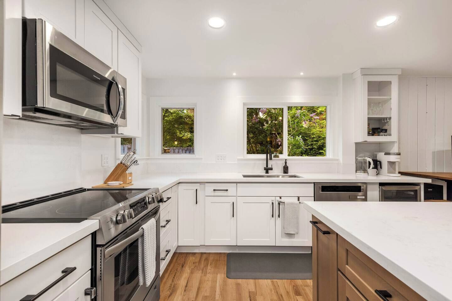 Una cocina moderna con armarios blancos, estufa de acero inoxidable, microondas y ventana con vistas a zonas verdes.