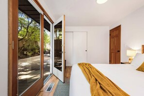 A bedroom with a bed, a wooden door, a white wardrobe, and a sliding glass door leading to an outdoor area. - BRIGHT 3BR LAKE CITY RETREAT — PRIVATE DECK, HOT TUB & FIREPLACE (Seattle)