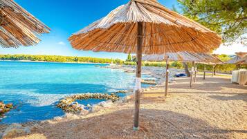 Une plage bordée de parasols en chaume, avec une eau d’un bleu limpide et un rivage rocheux.
