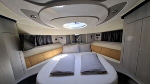 Een compact, goed verlicht interieur met een centraal bed, ingebouwde zithoek en een dakraam.